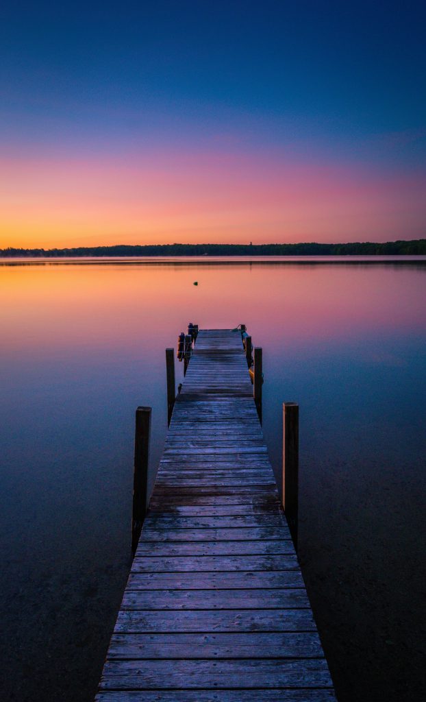 Empty wooden dock extending into a calm lake at sunrise, symbolizing loneliness, emotional disconnection, reflection, and the search for meaningful human connection.