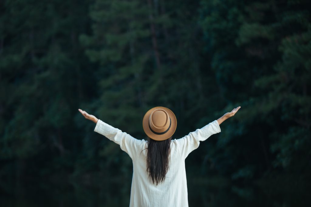 Woman standing with arms outstretched, eyes closed, appearing calm and grounded outdoors.