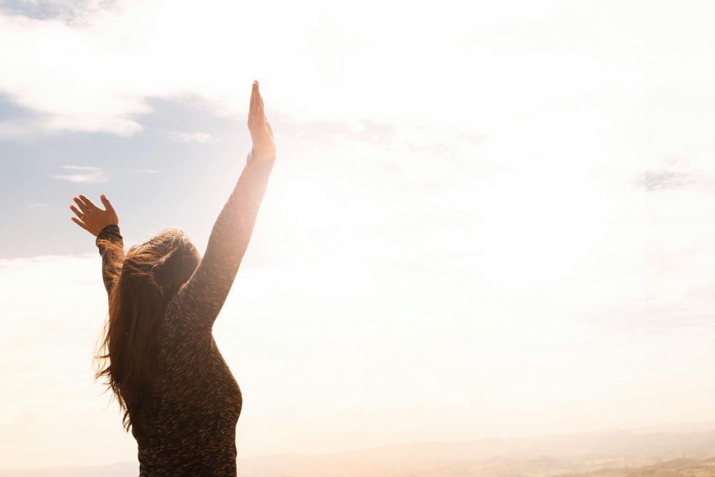 A woman standing with her arms open, facing the sunlight in a calm outdoor setting.