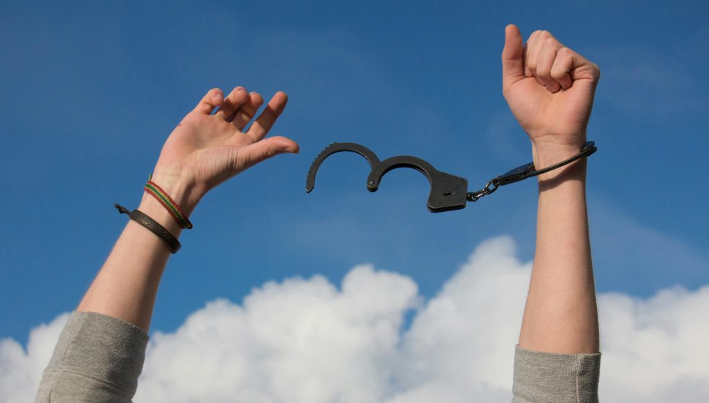 Hands breaking free from metal handcuffs, wrists separating as the cuffs open, symbolizing recovery, autonomy, and reclaiming choice after trauma